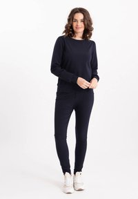 Marineblauwe sweatshirt met lange mouwen, bijpassende marineblauwe leggings, een gladde textuur en een casual pasvorm, gecombineerd met witte sportieve sneakers.