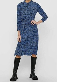 Vestito blu di lunghezza media con stampa leopardata nera, maniche lunghe, vita cinte con un fiocco, abbinato a stivali neri fino al ginocchio.