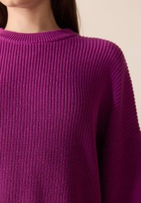 Fioletowy sweter z dzianiny o prążkowanej fakturze, z szerokim okrągłym dekoltem i luźnymi rękawami. Miękki materiał o przytulnym wyglądzie.