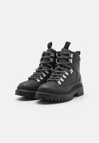 Botas de senderismo negras de cuero, con una suela resistente, ojales plateados y gruesos cordones negros y blancos con un diseño de bucle.