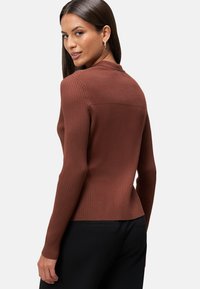 Braun gestreiftes Langarmoberteil mit einer eng anliegenden Silhouette, ausgestattet mit einem hohen Ausschnitt und einem strukturierten Strickmuster. Trägt man mit schwarzen Hosen.