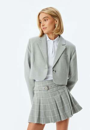 Grijze cropped blazer met een enkele knoop en een patchzak, gecombineerd met een grijze geruite geplooide rok met een riem en metalen gesp.