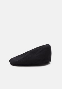 Casquette plate en laine noire avec une texture lisse et une silhouette incurvée. Présente des détails de surpiqûres subtils sur les côtés.