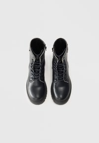 Botas de tornozelo em couro preto com detalhes em tachas, fechamento com zíper e atacadores na frente. Sola de borracha grossa e acabamento texturizado.