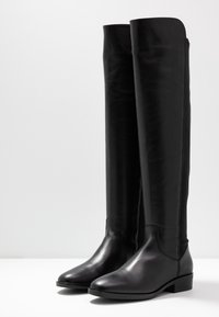 Bottes noires en cuir montant jusqu'au genou, avec une texture lisse, un bout arrondi, un petit talon empilé et un design minimaliste sans éléments métalliques visibles ni accents.