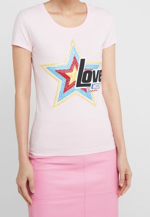 Kobieta ubrana w jasnoróżowy t-shirt z wielokolorową gwiazdą i tekstem "Love Moschino", w połączeniu z różową spódnicą.