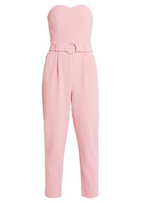 Combinaison rose sans bretelles avec un corsage ajusté et une taille ceinturée ornée d'une boucle circulaire argentée, jambes fuselées et texture de tissu lisse.