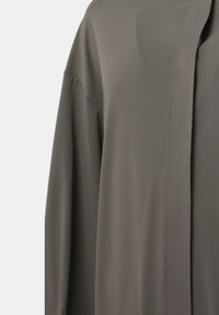 Camicia a maniche lunghe, leggera, in un verde oliva opaco. Tessuto elegante con una texture liscia e design minimalista; senza bottoni o decorazioni visibili.