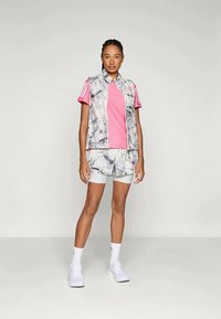 Sportowy strój składający się z jasnoszarej i białej kamizelki w wzory, różowej bluzki oraz dopasowanych szortów w ten sam wzór, uzupełniony białymi butami i skarpetkami.