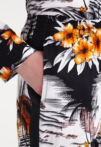 Blouse à manches courtes avec une base noire ornée d'imprimés tropicaux blancs et de fleurs oranges. Comprend une taille élastique et des poches latérales.