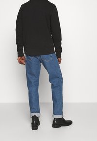 Schwarzer Sweatshirt mit Rundhalsausschnitt, kombiniert mit hochgekrempelten blauen Jeans und schwarzen Chelsea-Stiefeln, die einen lässigen Schnitt und Stil präsentieren.