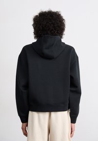 Hoodie cropped preto com capuz, apresentando uma textura suave, mangas largas e bainha canelada. Design simples sem logotipos ou padrões visíveis.