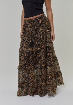 Jupe longue à volants en tissu léger, avec un imprimé léopard en marron et noir, agrémentée d'accents dorés et de pampilles noires.