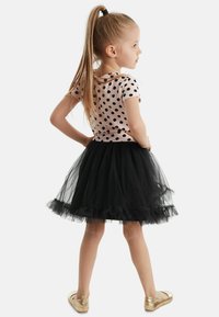 Vaaleanpunainen lyhythihainen paita, jossa on mustia pilkkuja, yhdistetty mustaan tüllihameeseen, jossa on röyhelöhelma, ja kullanvärisiin ballerinatossuihin.