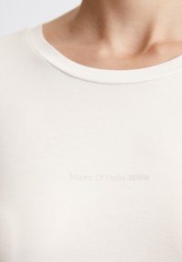Világos elefántcsont színű, puha pamutból készült póló, kerek nyakkivágással és diszkrét, a hemnél elhelyezett "Marc O'Polo DENIM" márkajellel.