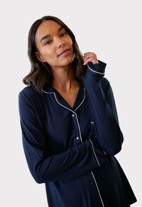 Granatowa koszula piżamowa z białymi lamówkami, z guzikami z przodu i długimi rękawami. Miękka tkanina o luźnym kroju z małą kieszonką na piersi.