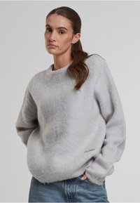 Grau, weich strukturierter Pullover mit Rundhalsausschnitt und überschnittenen Schultern, mit subtilen Nähten am Saum. Getragen mit blauen Jeans.