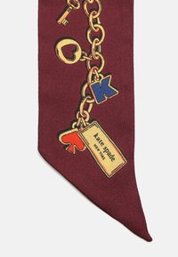Corbata de seda burdeos con un patrón de cadenas doradas que incluyen un llavero, un corazón y charms con letras, y una etiqueta que lleva el texto "kate spade" en negro.