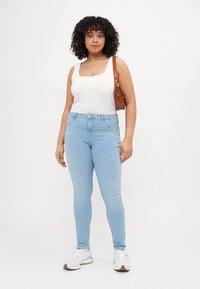 Light blue skinny jeans with a high waist, paired with a white tank top and white sneakers. Brown strap bag adds contrast. Smooth texture.