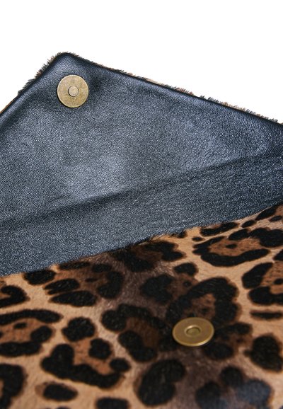 Sac imprimé léopard avec un rabat en cuir noir et des fermetures magnétiques en laiton ouvert sur fond blanc.