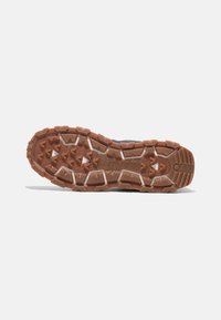 Suola di scarpa da trail running con una robusta gomma marrone, caratterizzata da tasselli multi-direzionali per una migliore aderenza, superficie testurizzata e dettagli di durabilità.