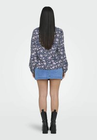 Blus med blommönster i blå och lila ton, kombinerad med en ljus denim-minikjol. Modellen bär svarta kraftiga klackstövlar.
