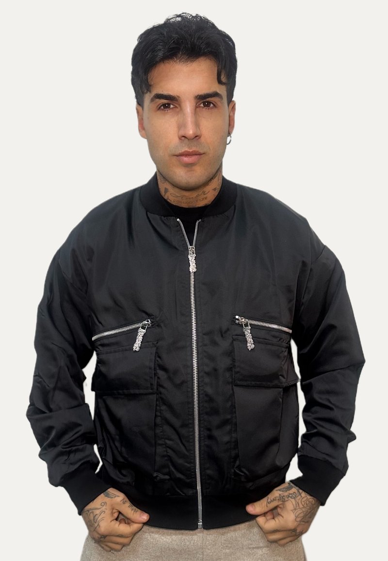 Giacca bomber nera in tessuto liscio, con due tasche sul petto con cerniera, polsini e collo a costine, chiusura frontale con zip.