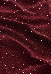 Bordeauxfarbiger Stoff mit gerippter Textur, der mit verstreuten silbernen Pailletten versehen ist, die ein gepunktetes Muster über die Oberfläche bilden.