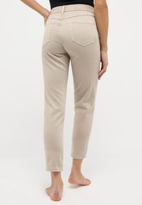 Pantalones ajustados beige de talle medio, con dos bolsillos traseros y una textura de tela suave. Longitud recortada por encima del tobillo.