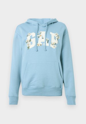 Lys blå hettegenser med frontlommekenguru, snorer og "GAP"-tekst utsmykket med hvite tusenfrydblomster på brystet.