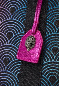 Svart tyg med blå vågmönster som har en klarrosa läderetikett präglad med en dekorativ silverdesign och en svart accent.