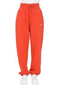 Pantalones de chándal rojos con una cintura elástica alta, cordón ajustable, tobillos acampanados y un pequeño logotipo blanco de Nike en el muslo izquierdo.