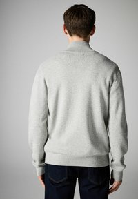 Hellgrauer Strickpullover mit hohem Kragen, gerippten Bündchen und Saum. Figurumspielendes Design, strukturierter Stoff und minimale Muster auf der Rückseite.