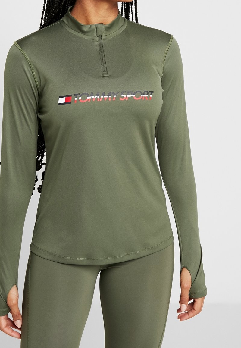 Olivgrünes, sportliches Langarmshirt mit halbem Reißverschluss am Kragen und "TOMMY SPORT"-Logo auf der Brust. Texturiertes, elastisches Material.