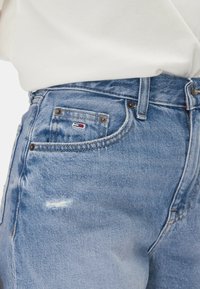 I jeans di denim blu chiaro presentano un classico design a cinque tasche con un dettaglio consumato sul davanti. Includono un piccolo etichetta con logo sulla tasca posteriore.