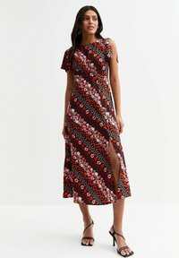 Vestido maxi en negro con estampados florales rojos y de lunares; presenta un diseño diagonal, una abertura lateral y mangas cortas con volantes.