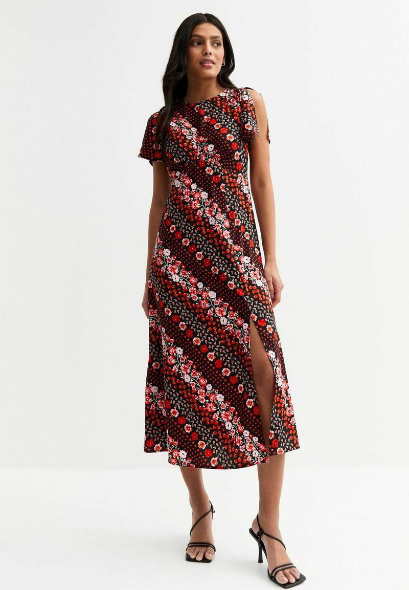 Vestido maxi en negro con estampados florales rojos y de lunares; presenta un diseño diagonal, una abertura lateral y mangas cortas con volantes.