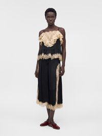 Femme portant un pantalon noir à jambes larges et un haut sans manches assorti avec des détails en dentelle beige, assorti à des chaussures plates rouges.