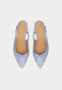 Világoskék hegyes orrú, pántos lapos cipőpár kis masnival és aranyozott fűzővéggel, látható átlyukasztott barna talpbetéttel.