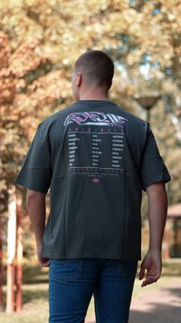 Mørkegrå oversized t-skjorte med grafisk trykk på ryggen med bynavn i rosa, kort erm, og en avslappet passform.