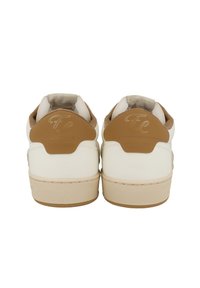 White leather sneakers with a tan rubber heel tab and a textured back. Features a beige sole and subtle logo on the heel.