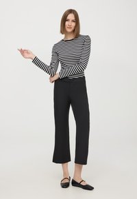 Pantaloni neri a vita alta abbinati a una maglietta a maniche lunghe a righe bianche e nere; entrambi presentano texture lisce e design aderenti. Scarpe nere basse completano l'outfit.