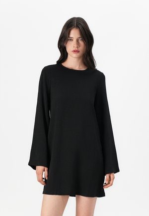 Svart langermet kjole med rund hals, med en avslappet passform og jevn tekstur, som ender over midt på låret. Enkel og minimalistisk design.