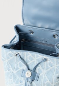 Τσαντάκι από ανοιχτό μπλε ύφασμα με υφή γεωμετρικού μοτίβου, που διαθέτει εσωτερικό από λείο δέρμα και ασημί μεταλλικά διακοσμητικά.