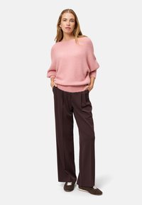 Jasnoróżowy sweter z mieszanki wełny o luźnym kroju i prążkowanym dole, zestawiony z ciemnobrązowymi szerokimi spodniami. Brązowe sneakersy dopełniają całość.