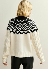Cream knitted sweater with black geometric pattern on the yoke; features textured cable-knit sleeves and ribbed hem for warmth.