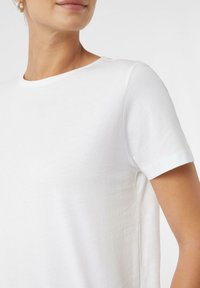 T-shirt blanc à manches courtes en coton doux, avec un col rond et une coupe décontractée, présentant une texture lisse et des lignes épurées.
