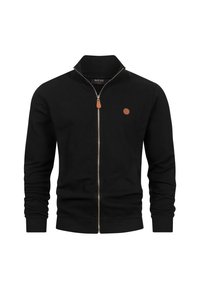 Chaqueta negra con cremallera y textura acanalada, cuello alto y detalles en cuero. Presenta un logo circular en el pecho.