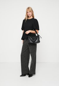 Top preto texturizado com mangas bufantes, calças largas cinzas com padrão e uma bolsa de couro preta com alça franzida.