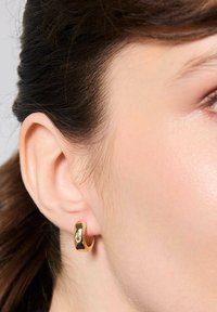 Złota kolczyk w formie obręczy o gładkim, zaokrąglonym kształcie z akcentem w postaci kamienia szlachetnego. Kolczyk ma polerowane wykończenie i nowoczesny, minimalistyczny kształt.